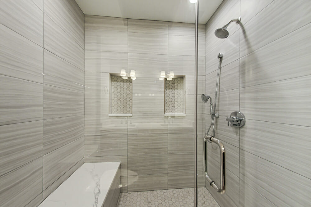 douche à l'italienne avec banc et carreaux de marbre sur les murs et étagères encastrées et porte vitrée après rénovation