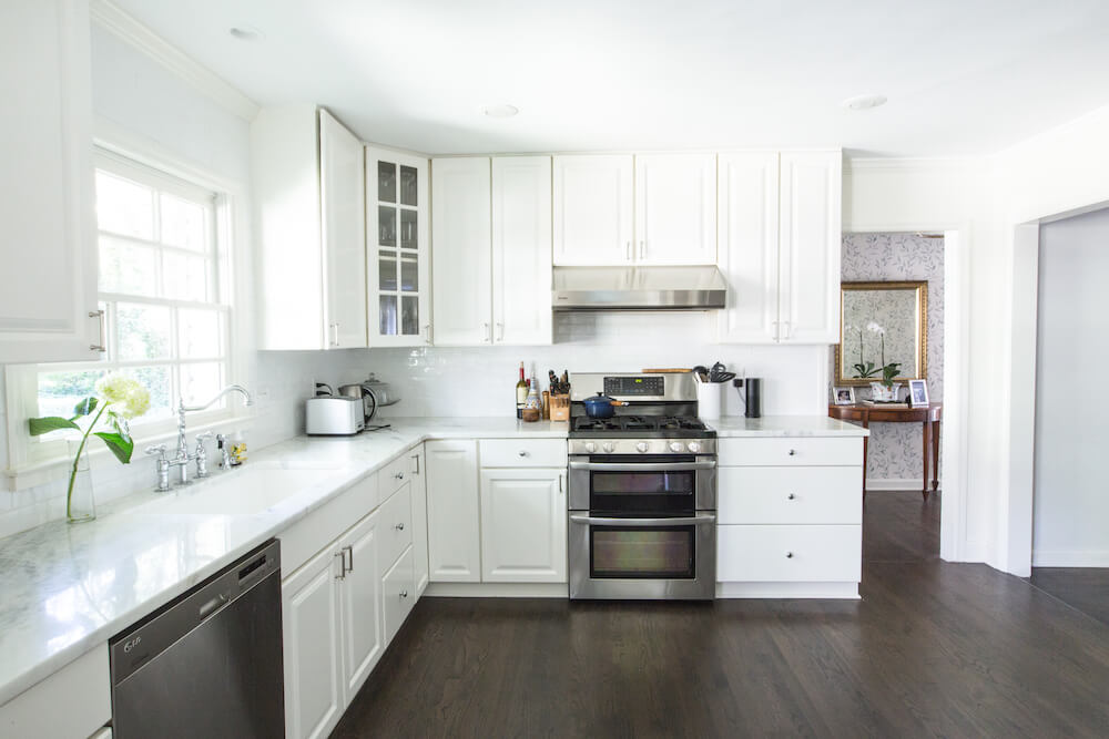 Comptoirs en marbre blanc, armoires blanches et planchers de bois franc foncé dans la cuisine
