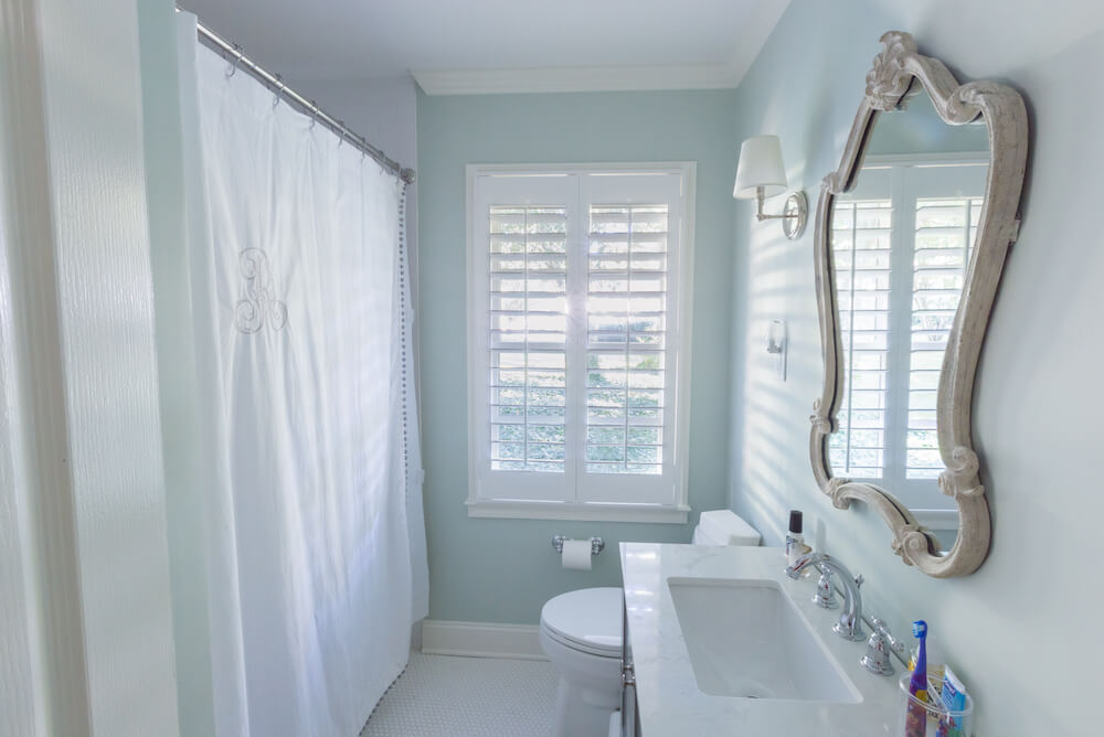 Salle de bain avec murs bleu clair, sol blanc, rideau de douche blanc et miroir décoratif
