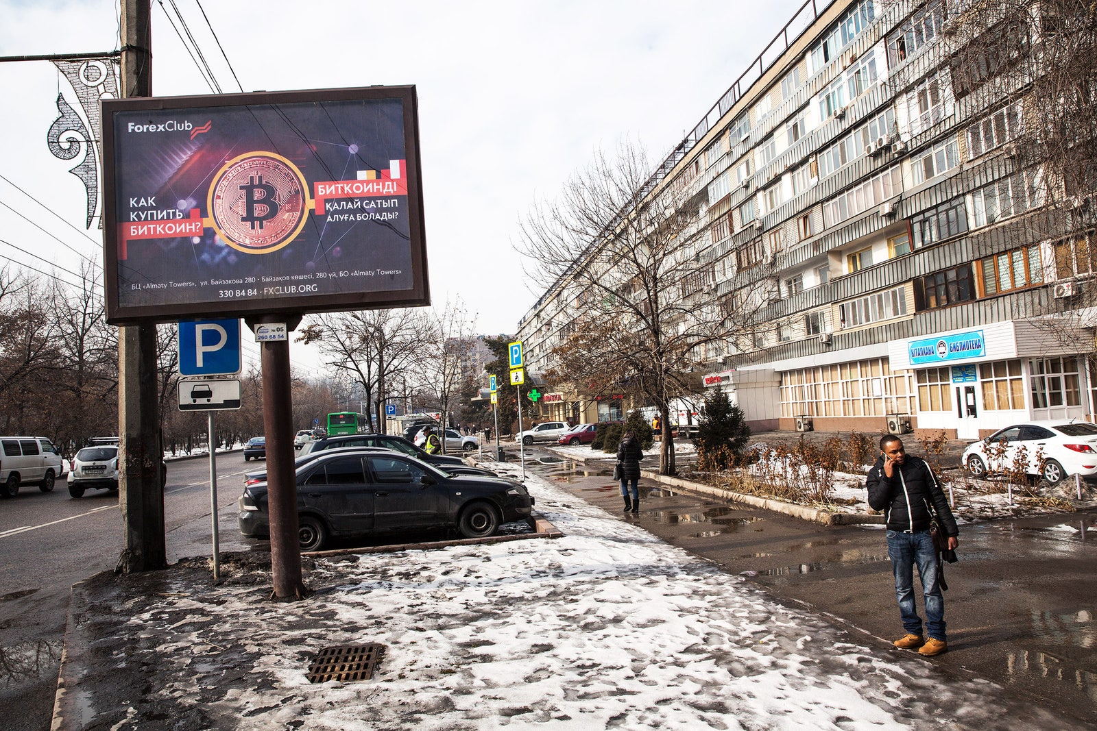 Un homme passe un appel téléphonique à côté d'un panneau d'affichage Bitcoin à l'extérieur un jour de neige au Kazakhstan